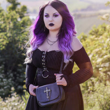 Load image into Gallery viewer, Model wearing a goth outfit holding the gothx don&#39;t cross me vegan shoulder bag across their body with the bag facing forward to highlight the studded cross chain centrepiece.
