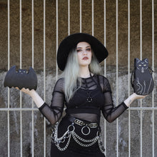 Load image into Gallery viewer, Model with silver hair wearing a goth outfit is holding the gothx pagan black cat vegan shoulder bag out on their right hand and the gothx bat bag on their left hand. The bag is facing forward to highlight the embroidery details including a pentagram collar, yellow eyes and paws.
