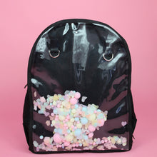 Load image into Gallery viewer, The Kawaii Black & Clear Window Vegan Ita Backpack on a pastel pink background. The bag is facing forward filled with pastel confetti and pom poms to highlight the clear display window and inside D rings to hang things from.