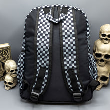 Load image into Gallery viewer,  The Grey Checkerboard Backpack sat on a grey background with a palmistry guide book and two skull stack on the right and a phrenology guide candle and three skull stack on the left. The vegan friendly bag is facing away from the camera to highlight the plain black back, the two side elasticated pockets, the top handle and the two adjustable padded shoulder straps.
