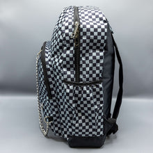 Load image into Gallery viewer,  The Grey Checkerboard Backpack sat on a grey background. The vegan friendly bag is facing left to highlight the grey and black check print, two front zip pockets, two elasticated side pockets, main top double zip pocket and silver draping decorative chain.
