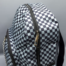 Load image into Gallery viewer, Close up of the Grey Checkerboard Backpack sat on a grey background. The vegan friendly bag is facing forward to highlight the grey and black check print, two front zip pockets, two elasticated side pockets, main top double zip pocket and silver draping decorative chain.
