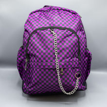 Load image into Gallery viewer, The Purple Checkerboard Backpack sat on a grey background. The vegan friendly bag is facing forward to highlight the purple and black check print, two front zip pockets, two elasticated side pockets, main top double zip pocket and silver draping decorative chain.
