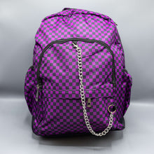 Load image into Gallery viewer, The Purple Checkerboard Backpack sat on a grey background. The vegan friendly bag is facing forward to highlight the purple and black check print, two front zip pockets, two elasticated side pockets, main top double zip pocket and silver draping decorative chain.