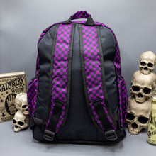 Load image into Gallery viewer, The Purple Checkerboard Backpack sat on a grey background with a palmistry guide book and two skull stack on the right and a phrenology guide candle and three skull stack on the left. The vegan friendly bag is facing away from the camera to highlight the plain black back, the two side elasticated pockets, the top handle and the two adjustable padded shoulder straps.