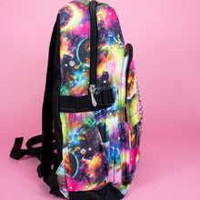 Load image into Gallery viewer, The pink and purple space galaxy vegan backpack sat on a pink studio background. The backpack is facing right to highlight the multicoloured space/planet/galaxy print, two zip pockets, two elastic side pockets and detachable silver chain.
