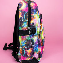 Load image into Gallery viewer, The pink and purple space galaxy vegan backpack sat on a pink studio background. The backpack is facing right to highlight the multicoloured space/planet/galaxy print, two zip pockets, two elastic side pockets and detachable silver chain.