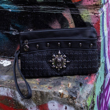Load image into Gallery viewer, The gothx black skull vegan clutch bag on an alternative colourful graffiti brick wall outside. The vegan clutch bag is facing forward to highlight the skull embossed vegan black leather, the crystal stud skull centrepiece, zip pocket and skull studs.