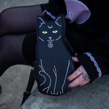 Load image into Gallery viewer, The gothx pagan black cat vegan shoulder bag resting next to a model wearing an all black hello kitty outfit. The bag is facing forward to highlight the embroidery details including a pentagram collar, yellow eyes and paws.