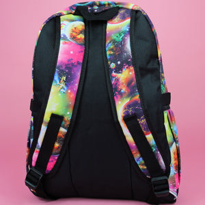 The pink and purple space galaxy vegan backpack sat on a pink studio background. The backpack is facing away from the camera to highlight the two side pockets, the plain black back and two padded adjustable shoulder straps.