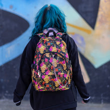 Load image into Gallery viewer, Model walking away wearing the floral gold skull nylon chain vegan backpack. The bag is facing the camera to highlight the flowers and skulls print, two zipped pockets, two elastic side pockets and detachable decorative silver chain.