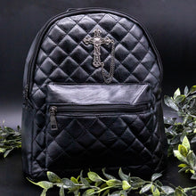 Load image into Gallery viewer, The GothX quilted cross vegan mini backpack on a black studio background with black roses and leaves surrounding it. Quilted front detailing with a studded cross with hanging chain appliqué and zip front pocket. Black vegan leather with gunmetal grey detailing. The bag is facing forward to show off the front details.