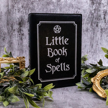 Load image into Gallery viewer, The gothx little book of spells vegan shoulder bag on a grey background with green foliage and gold frames surrounding it. The witchy inspired vegan leather bag is facing towards the camera to highlight the white printed design of a pentagram, framing and text reading little book of spells.