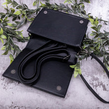 Load image into Gallery viewer, The gothx little book of spells vegan shoulder bag on a grey background with green foliage surrounding it. The bag is laying open to highlight the two magnetic clip close, an adjustable detachable shoulder strap and detachable wrist strap.
