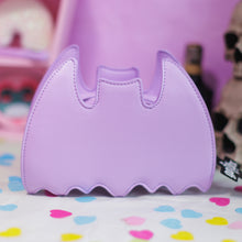 Load image into Gallery viewer, The GothX LIMITED EDITION Pastel Lilac Purple Bat Vegan Shoulder Bag on a pastel purple background with multicoloured confetti, pastel pink coffin shelving and black skull bottles surrounding it. The bag is facing away to highlight the plain pastel purple back.