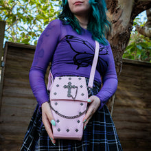 Load image into Gallery viewer, GothX Pastel Pink Mini Coffin Vegan Cross Body Bag being held up by an alternative goth model. The bag is facing forward to highlight the cross studs, cross & chain centrepiece, detachable chain and detachable adjustable shoulder strap.