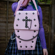 Load image into Gallery viewer, GothX Pastel Pink Mini Coffin Vegan Cross Body Bag being held up by an alternative goth model. The bag is facing forward to highlight the cross studs, cross &amp; chain centrepiece and detachable chain.
