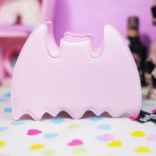 Load image into Gallery viewer, The GothX Pastel Pink Bat Vegan Shoulder Bag on a pastel purple background with multicoloured confetti, pastel pink coffin shelving and black skull bottles surrounding it. The bag is facing away to highlight the plain pastel pink back.
