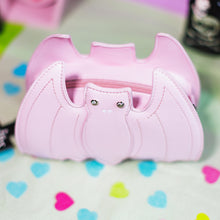 Load image into Gallery viewer, The GothX LIMITED EDITION Pastel Pink Bat Vegan Shoulder Bag on a pastel purple background with multicoloured confetti, pastel pink coffin shelving and black skull bottles surrounding it. The bag is facing forward to highlight the embroidered detailing and crystal eyes.