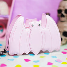 Load image into Gallery viewer, The GothX Pastel Pink Bat Vegan Shoulder Bag on a pastel purple background with multicoloured confetti, pastel pink coffin shelving and black skull bottles surrounding it. The bag is facing forward to highlight the embroidered detailing and crystal eyes.
