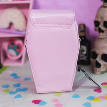 Load image into Gallery viewer, The GothX Pastel Pink Mini Coffin Vegan Cross Body Bag on a pastel purple background with pastel pink coffin shelving, skulls and black faux skull poison bottles in the background. The bag is facing away to highlight the plain pastel pink vegan leather back.
