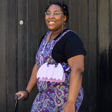 Load image into Gallery viewer, The GothX Pastel Lilac Purple Bat Vegan Shoulder Bag being modelled on a shoulder of someone wearing Run & Fly purple paisley pinafore. The vegan leather pastel bag is facing forward to highlight the embroidered detailing and crystal eyes.