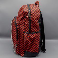 Load image into Gallery viewer, The Red Checkerboard Backpack sat on a grey background. The vegan friendly bag is facing left to highlight the red and black check print, two front zip pockets, two elasticated side pockets, main top double zip pocket and silver draping decorative chain.