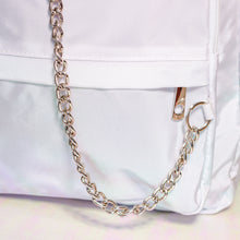 Load image into Gallery viewer, The white nylon vegan backpack with chain on an iridescent background. Close up of the detachable silver chain and front zip pocket detailing.