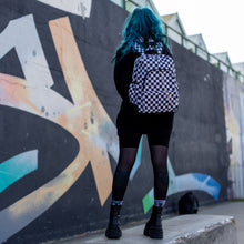 Load image into Gallery viewer, Model with blue hair wearing all black is stood in a skatepark near a graffiti wall wearing the chok white checker vegan backpack.