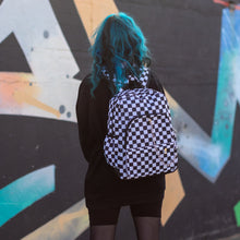 Load image into Gallery viewer, Model with blue hair wearing all black is stood in a skatepark near a graffiti wall wearing the chok white checker vegan backpack.
