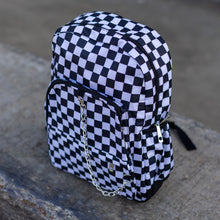 Load image into Gallery viewer, CHOK white checker vegan backpack sat on a skatepark bench. The bag is facing forward angled left to highlight the white and black checkered square print, silver detachable chain, two front zip pickets and two side elastic pockets.