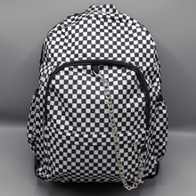 Load image into Gallery viewer, The White Checkerboard Backpack sat on a grey background. The vegan friendly bag features an all over mini black and white check print with black trim along the silver zips. The bag is facing forward to highlight the two front zip pockets, two side elasticated pockets, the top zip compartment, the top handle and the silver decorative detachable chain draping across the front.