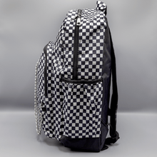 Load image into Gallery viewer, The White Checkerboard Backpack sat on a grey background. The vegan friendly bag features an all over mini black and white check print with black trim along the silver zips. The bag is facing left to highlight the two front zip pockets, two side elasticated pockets, the top zip compartment, the top handle and the silver decorative detachable chain draping across the front.