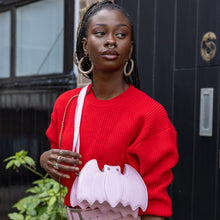 Load image into Gallery viewer, GothX Pastel Pink Bat Vegan Shoulder Bag being held by an alternative model wearing a pastel goth outfit. The bag is facing forward to highlight the embroidered detailing, silver faux crystal eyes and detachable adjustable strap.