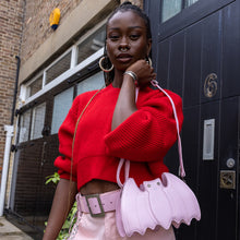 Load image into Gallery viewer, GothX Pastel Pink Bat Vegan Shoulder Bag being held by an alternative model wearing a pastel goth outfit. The bag is facing forward to highlight the embroidered detailing, silver faux crystal eyes and detachable adjustable strap.