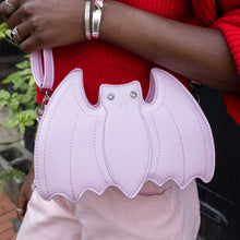 Load image into Gallery viewer, GothX Pastel Pink Bat Vegan Shoulder Bag being held by an alternative model wearing a pastel goth outfit. The bag is facing forward to highlight the embroidered detailing, silver faux crystal eyes and detachable adjustable strap.