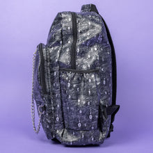 Load image into Gallery viewer, The Rustic Silver Spider Backpack sat on a purple background. The bag is facing left to highlight the two zip front pockets, two elasticated side pockets, the double zip main compartment with a silver draping chain across the front. The vegan friendly faux leather bag has 3d embossed spiders in varying sizes with brushed black and silver tones all over.
