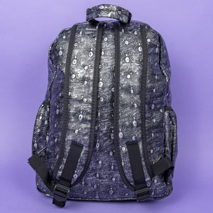 The Rustic Silver Spider Backpack sat on a purple background. The bag is facing away to highlight the two padded shoulder straps, the top handle and two elasticated side pockets. The vegan friendly faux leather bag has 3d embossed spiders in varying sizes with brushed black and silver tones all over.