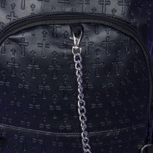 Load image into Gallery viewer, A close up of the Black Embossed Cross Backpack sat on a purple background. The backpack is facing forward to highlight the two front silver zip pockets, two elasticated side pockets, main double zip compartment and a silver decorative detachable silver chain draping across the front. The bag is made of vegan friendly leather with 3d embossed crosses in varying sizes all over.
