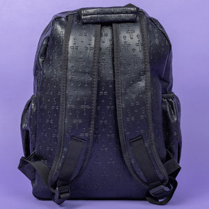 The Black Embossed Cross Backpack sat on a purple background. The backpack is facing away from the camera to highlight the two elasticated side pockets, padded shoulder straps and top handle. The bag is made of vegan friendly leather with 3d embossed crosses in varying sizes all over.