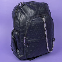 Load image into Gallery viewer, The Black Embossed Cross Backpack sat on a purple background. The backpack is facing forward angled slightly right to highlight the two front silver zip pockets, two elasticated side pockets, main double zip compartment and a silver decorative detachable silver chain draping across the front. The bag is made of vegan friendly leather with 3d embossed crosses in varying sizes all over.
