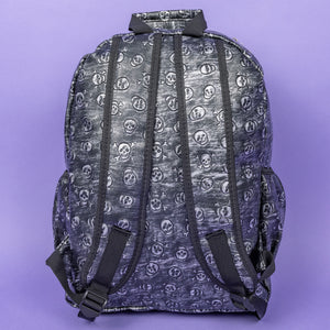 The Rustic Skulls Backpack sat on a purple background. The bag is facing away to highlight the two padded shoulder straps, two elasticated side pockets, main zip compartment and the top handle. All over the backpack is an embossed 3d texture skulls and skull and crossbones on a faux leather material in a brushed black and silver grunge style.