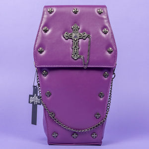 The GothX Purple Coffin Backpack. sat facing forward on a lilac background. The coffin bag in a sleek faux leather is a coffin shape with a magnetic close clip flap with a cross chain emblem in the centre, surrounding the coffin shape is mini metal cross studs. Draping across the front of a silver detachable decorative chain with the GothX black cross tag hanging to the left side.