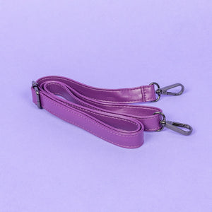 The GothX Purple Coffin Bag detachable adjustable strap with metal d rings and lobster clips laying folded on a lilac background.