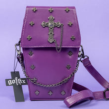 Load image into Gallery viewer, The GothX Purple Mini Coffin Bag sat facing forward on a lilac background. The coffin bag in a sleek faux leather is a coffin shape with a magnetic close clip flap with a cross chain emblem in the centre, surrounding the coffin shape is mini metal cross studs. Draping across the front of a silver detachable decorative chain with the GothX black cross tag hanging to the left side.
