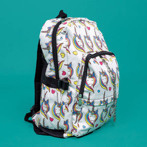 The Rainbow Unicorn Backpack sat facing right on a teal background. The vegan friendly backpack is a white canvas material with repeating kawaii cute unicorn heads with pink blue and yellow manes with hearts surrounding them. The bag is facing forward to highlight the front two zip pockets, the main zip compartment and silver draping decorative chain.