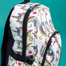 Load image into Gallery viewer, Close up of the Rainbow Unicorn Backpack sat facing right on a teal background. The vegan friendly backpack is a white canvas material with repeating kawaii cute unicorn heads with pink blue and yellow manes with hearts surrounding them. The bag is facing forward to highlight the front two zip pockets, the main zip compartment and silver draping decorative chain.
