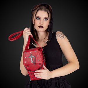 A gothic styled model with dark vampy red makeup wearing a goth black hooded dress holding the GothX Red Mini Coffin Bag to their chest and looking off to the right on a black background. The coffin bag is made with vegan friendly sleek red leather and features a detachable decorative metal chain with metal cross studding.