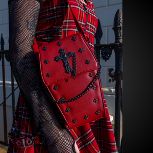 A goth model wearing an emo red tartan dress with the GothX Red Mini Coffin Bag on their shoulder. The coffin bag is made with vegan friendly sleek red leather and features a detachable decorative metal chain with metal cross studding.