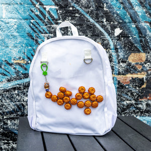 The White & Clear Window Ita Backpack sat on a wooden table in front of a graffiti wall. The bag is facing forward to highlight the clear front window filled with glittery pumpkins and two metal D rings with a keyring attached, two side elasticated pockets, main zip compartment and top handle. The vegan friendly bag is inspired by kawaii jfashion.